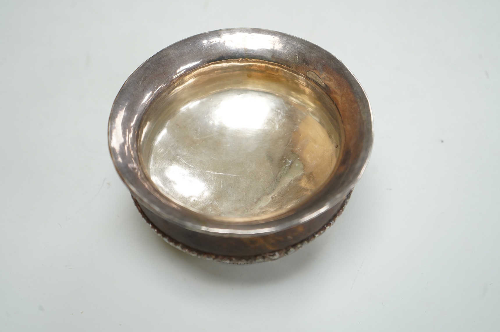 An antique Tibetan white metal mounted burl wood tsampa bowl, on a circular foot, diameter 99mm.